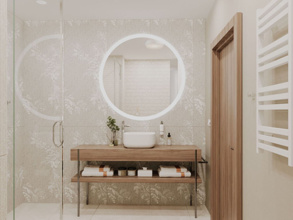 Nowoczesna łazienka w apartamencie Linea Mare w Kołobrzegu z drewnianą szafką pod umywalkę, okrągłym podświetlanym lustrem i jasną tapetą w delikatny wzór roślinny.